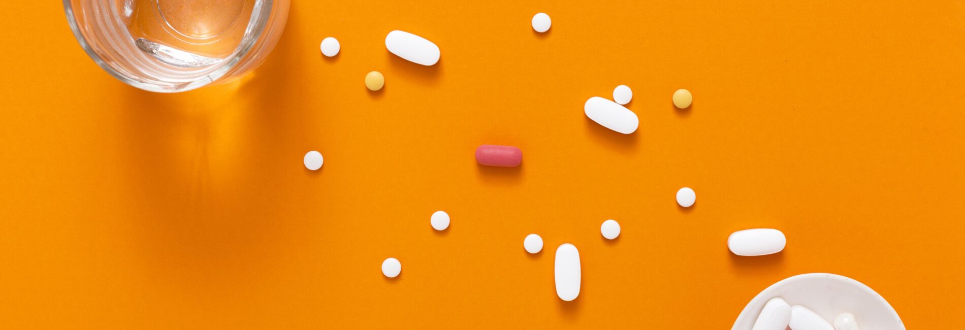 view from top down of a bowl of pills alongside a glass of water