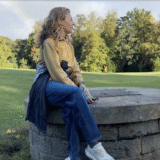 A picture of Clare Johnston seated on a stone well with a rainbow behind her